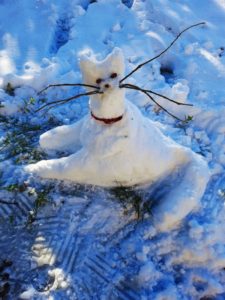 a cat built of snow with twigs for whiskers