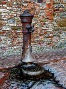 an example of ornate drinking water fountains in Italy, this one is an old rusty one with worn terracotta tiles at the base