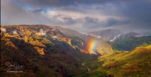 A beautiful landscape panoramic view of a mountainous landscape with light, shadows and part of a rainbow coming down to touch the ground.