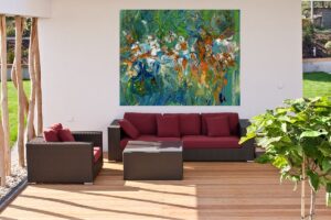 An outdoor seating area with a burgundy and brown sofa. On the wall, a large, bright and lively abstract painting featuring shades of green, gold, bronze and white.