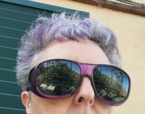 Top part of a woman's head, she has purple hilights in her gray hair. She is wearing amethyst coloured fitovers with dark polarized lenses
